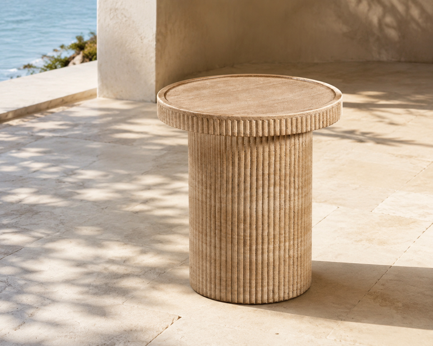 TOV Furniture Darcy faux-travertine round fluted side table on a sunlit coastal terrace